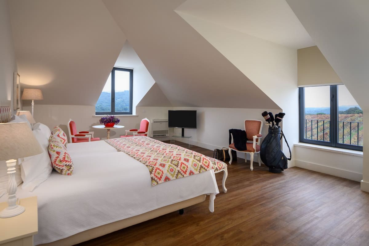 A bedroom with a large bed, a TV, a desk, and a chair. There is a window with a view of the mountains.