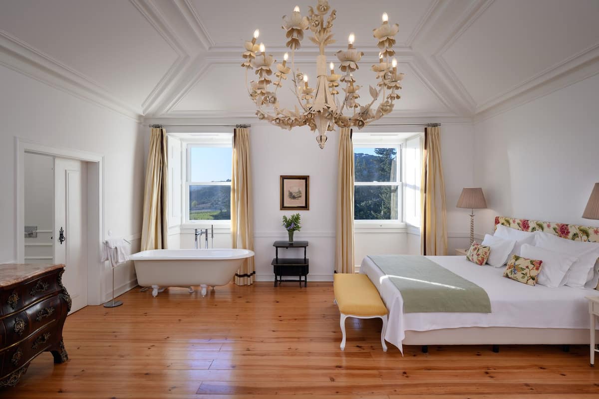 A classic bedroom with a large bed, a vintage clawfoot bathtub, and a chandelier.