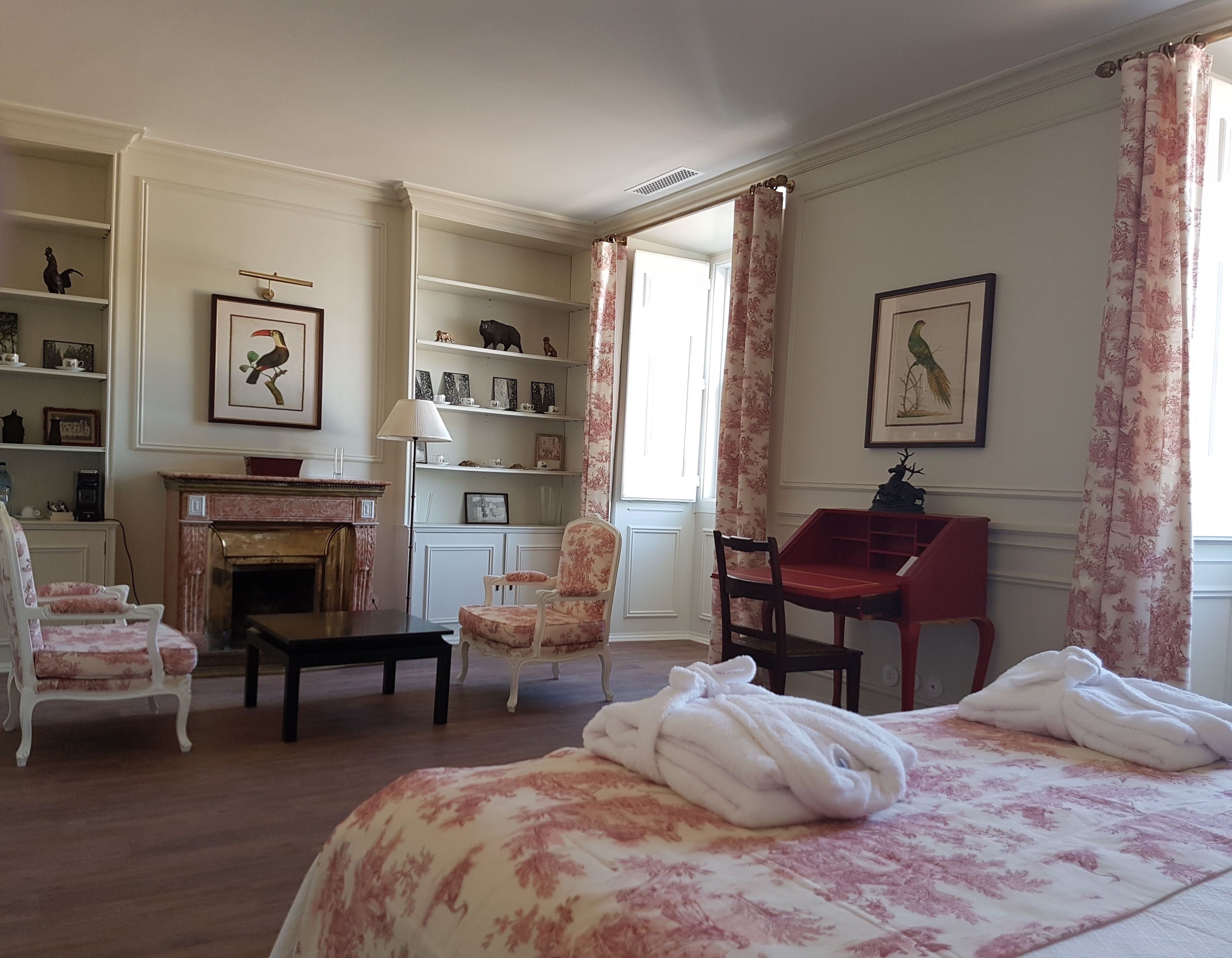 Una habitación con chimenea, cama con ropa de cama floral, escritorio y una silla.