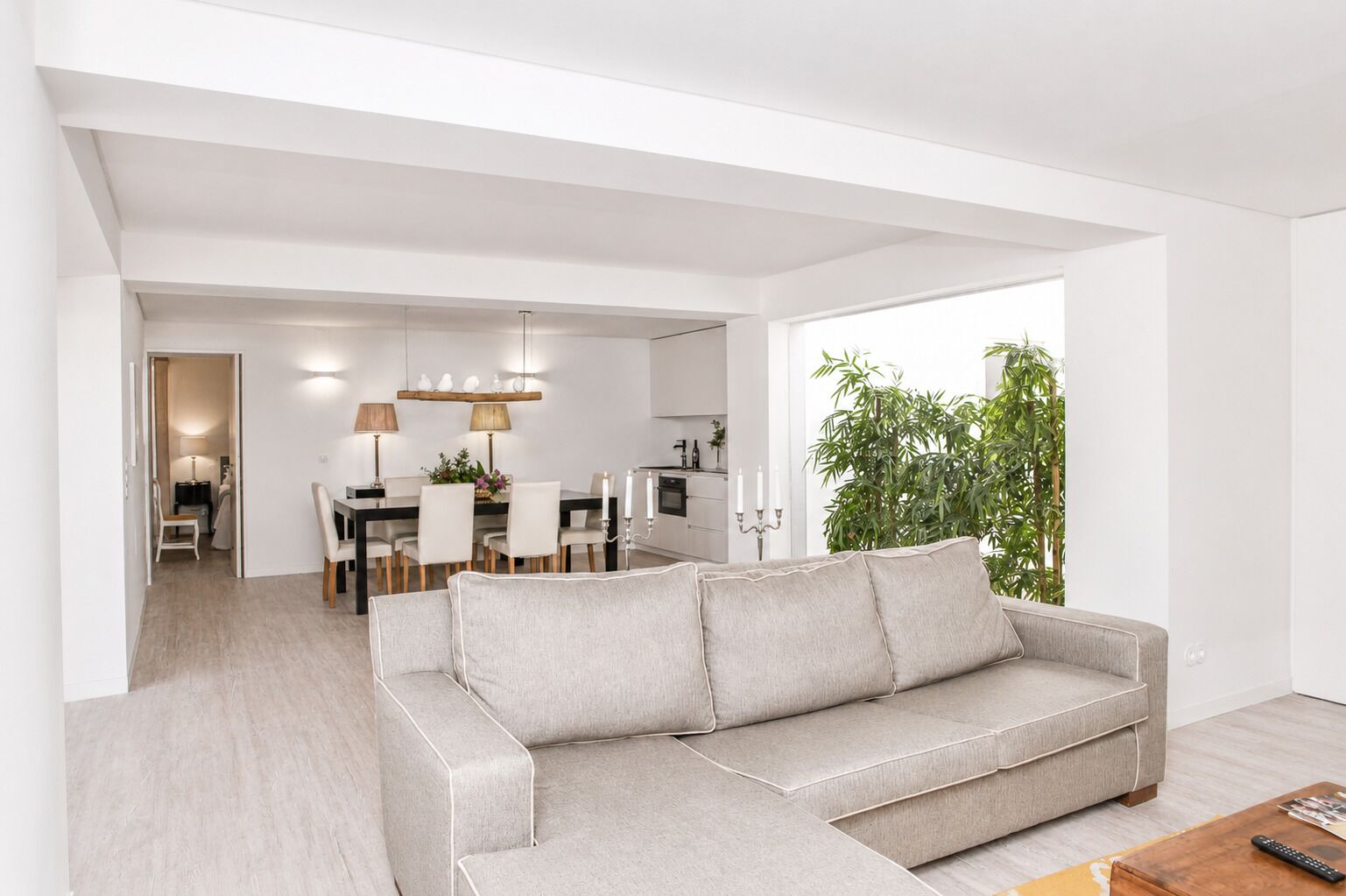 A modern living room with a grey sectional sofa, a dining area with a table and chairs, and a kitchen in the background.
