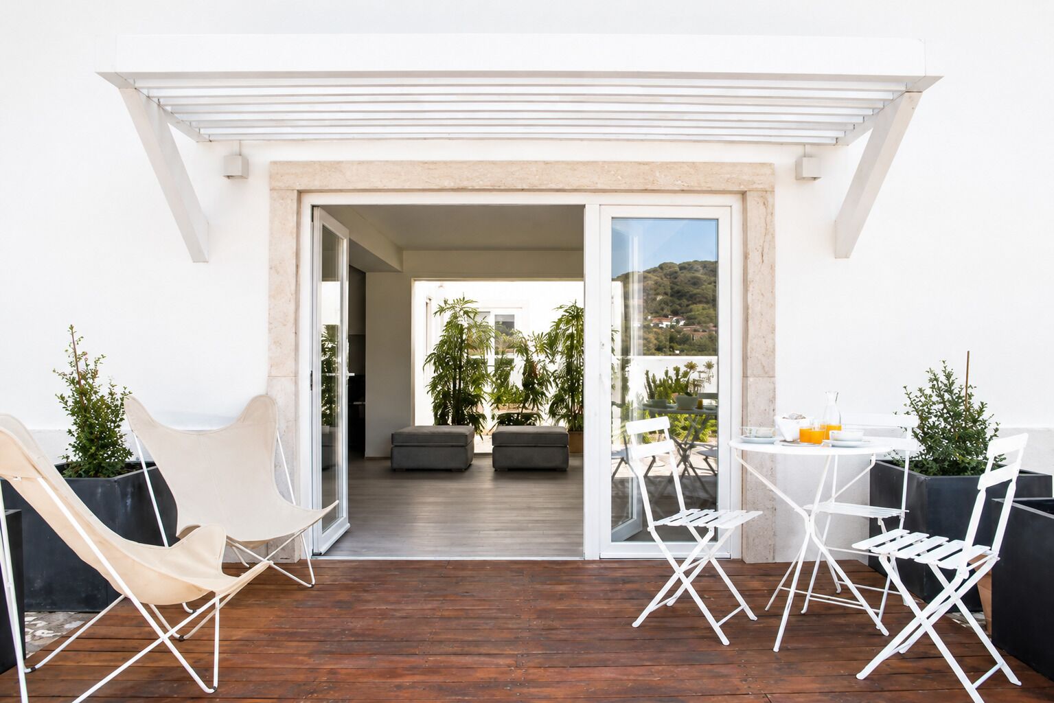 A modern outdoor patio with a wooden floor, white furniture, and potted plants.