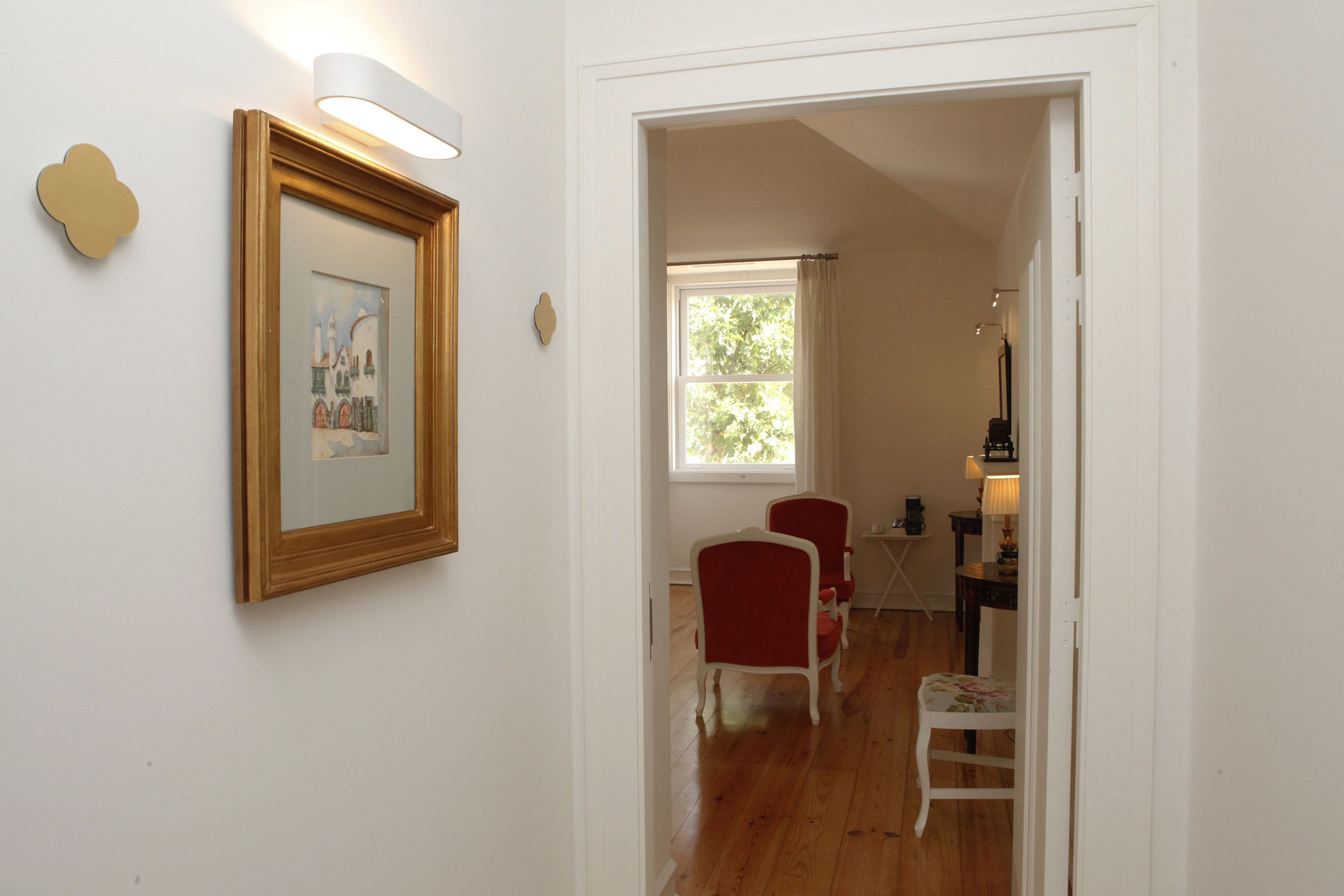 A hallway with a framed picture on the wall, a window with curtains, and a dining area with chairs and a table.