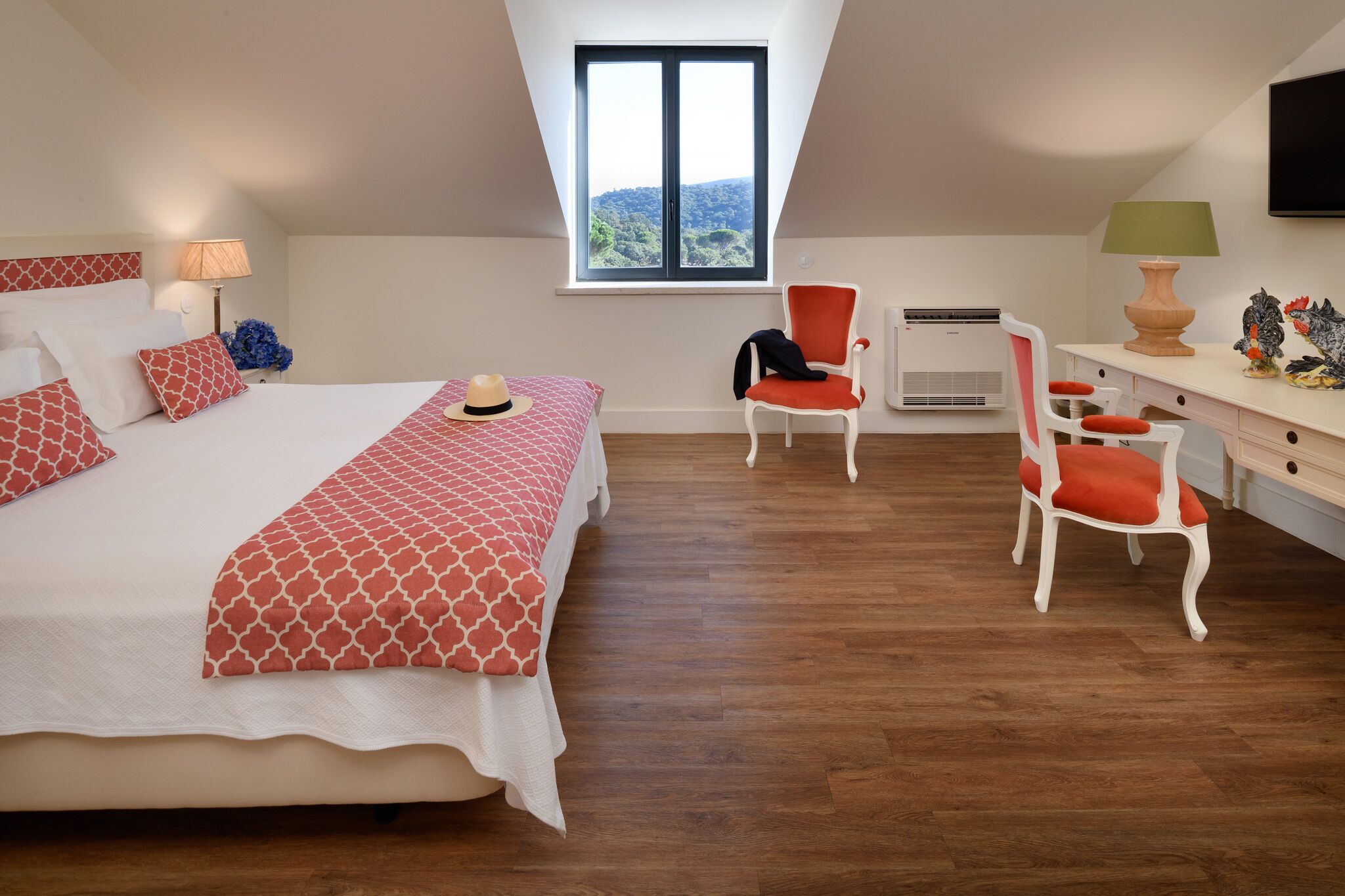 Een slaapkamer met een groot bed, een bureau en een stoel. Er is een raam met uitzicht op de omgeving.