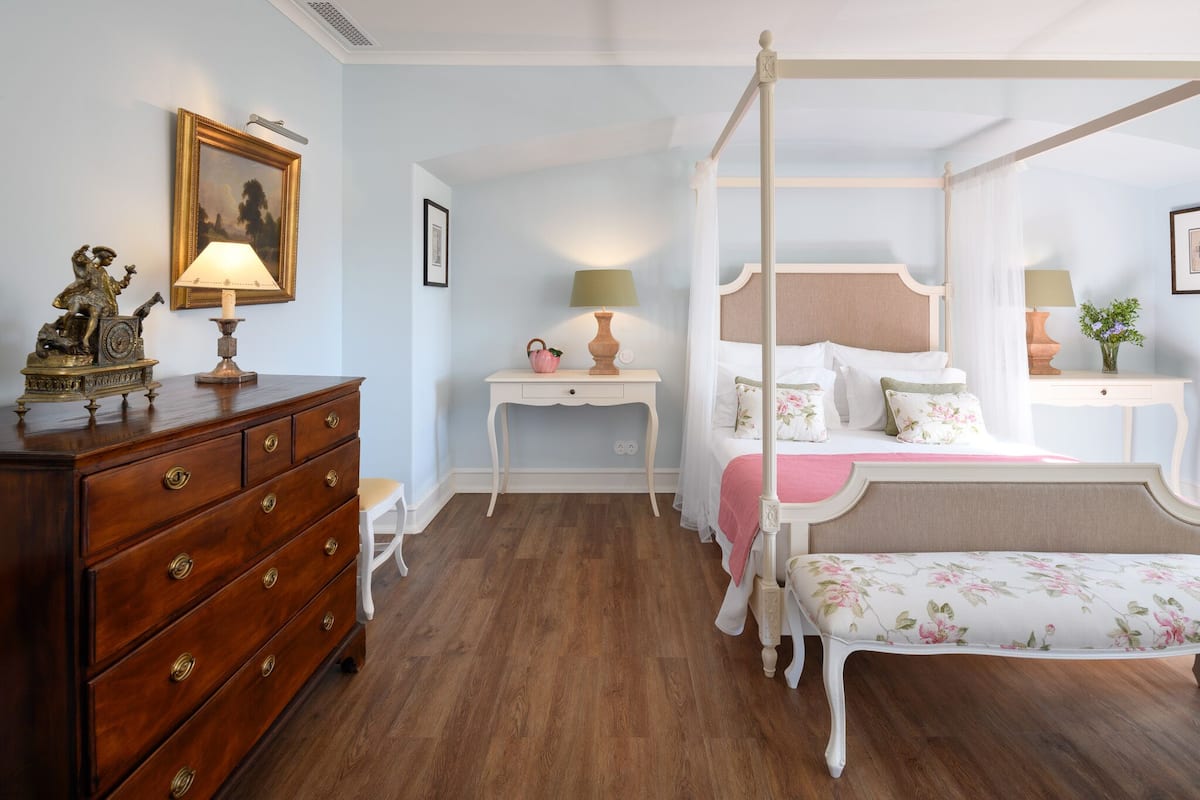 A bedroom with a four-poster bed, a wooden dresser, a nightstand, and a bench.