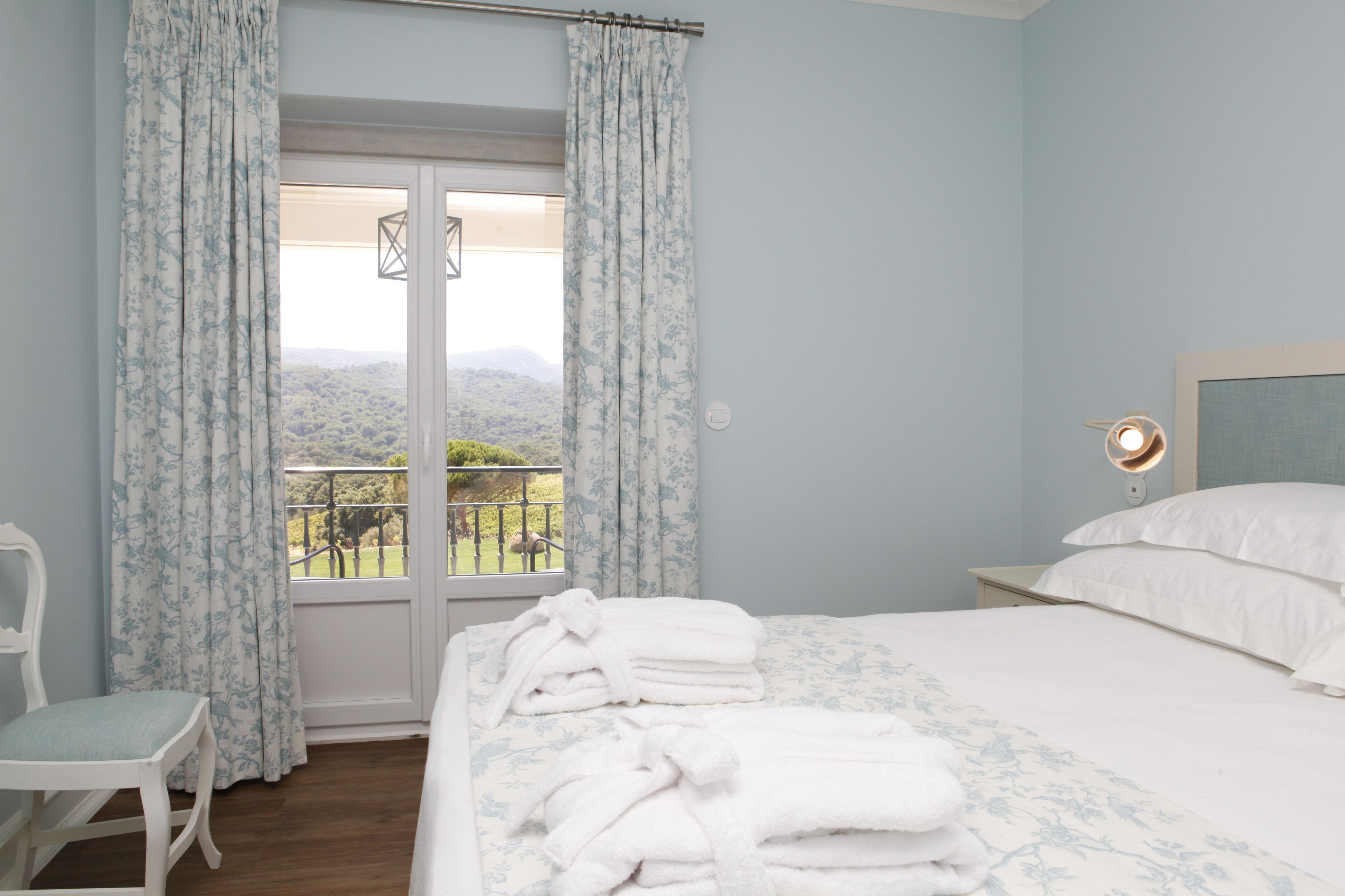A bedroom with a bed, a chair, a nightstand, and a view of a balcony with a railing.