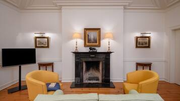 Una sala de estar con chimenea, dos sillones amarillos, un sofá verde, un televisor de pantalla plana y cuadros enmarcados en las paredes.