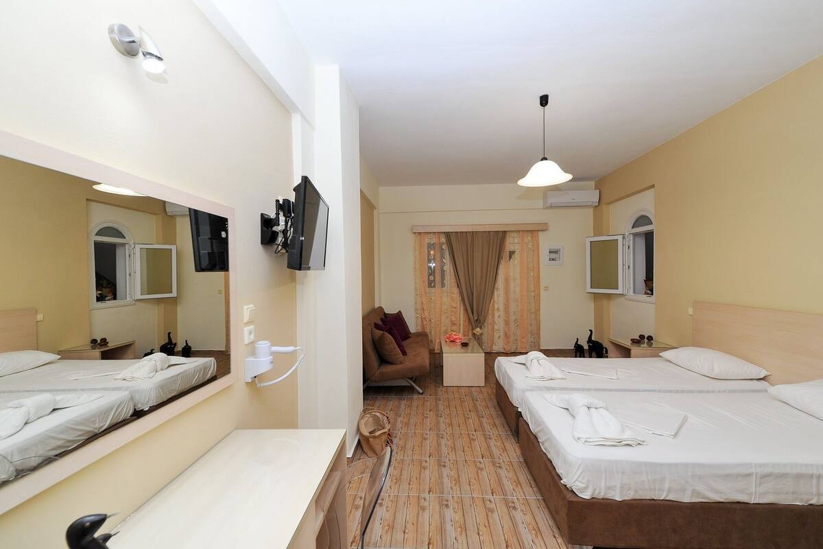 A hotel room with two beds, a desk, a chair, a mirror, a TV, and an air conditioning unit.