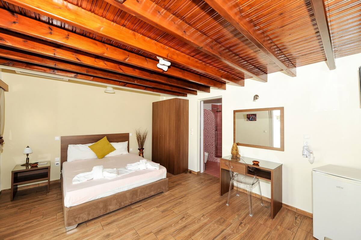 A bedroom with a wooden ceiling, a bed with white linens, a wooden desk, and a mirror.