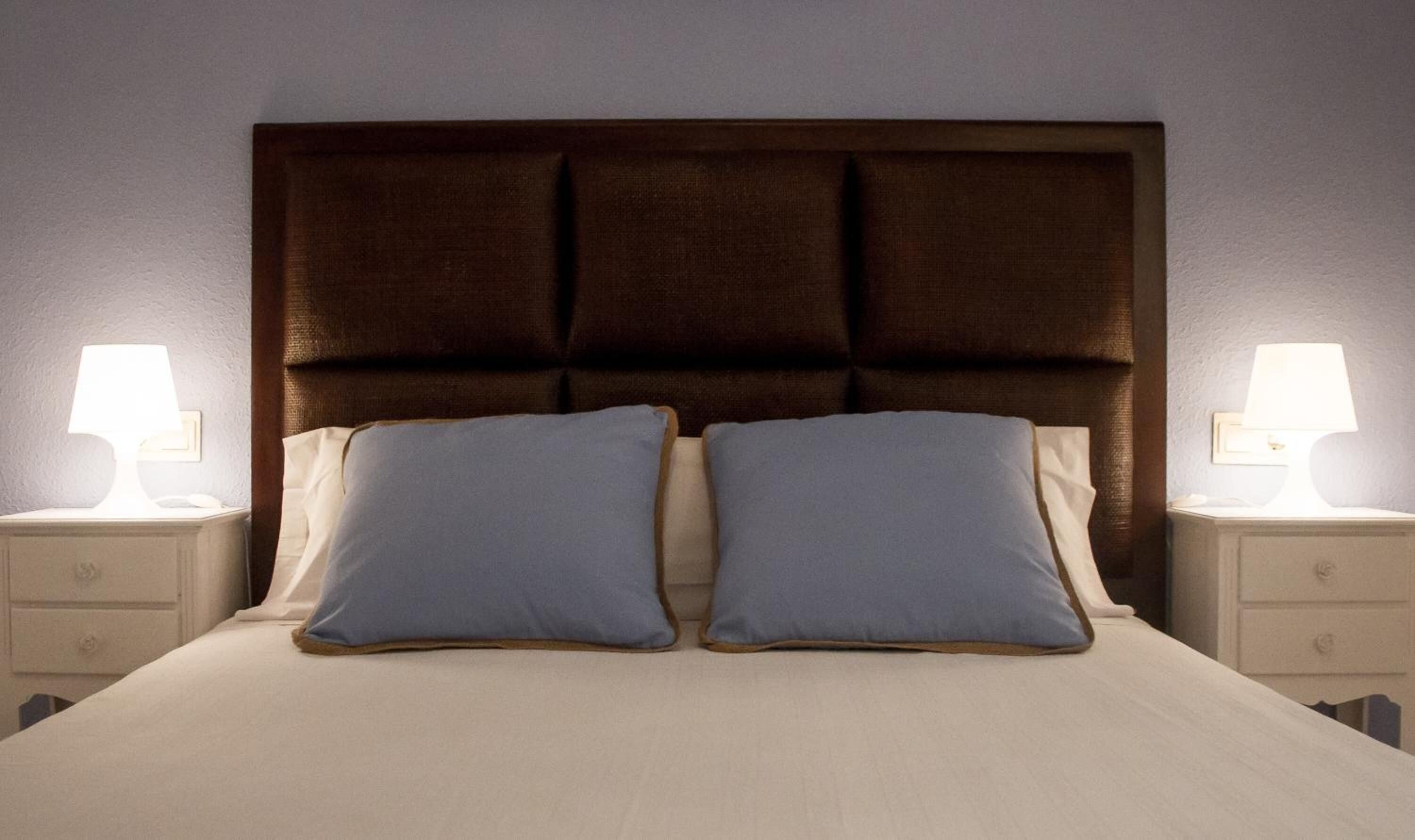 Una cama con cabecera oscura, dos almohadas y dos lámparas de noche.