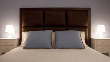 Una cama con cabecera oscura, dos almohadas y dos lámparas de noche.