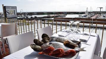 Une table à manger dressée avec des fruits de mer, sur une terrasse donnant sur une marina.