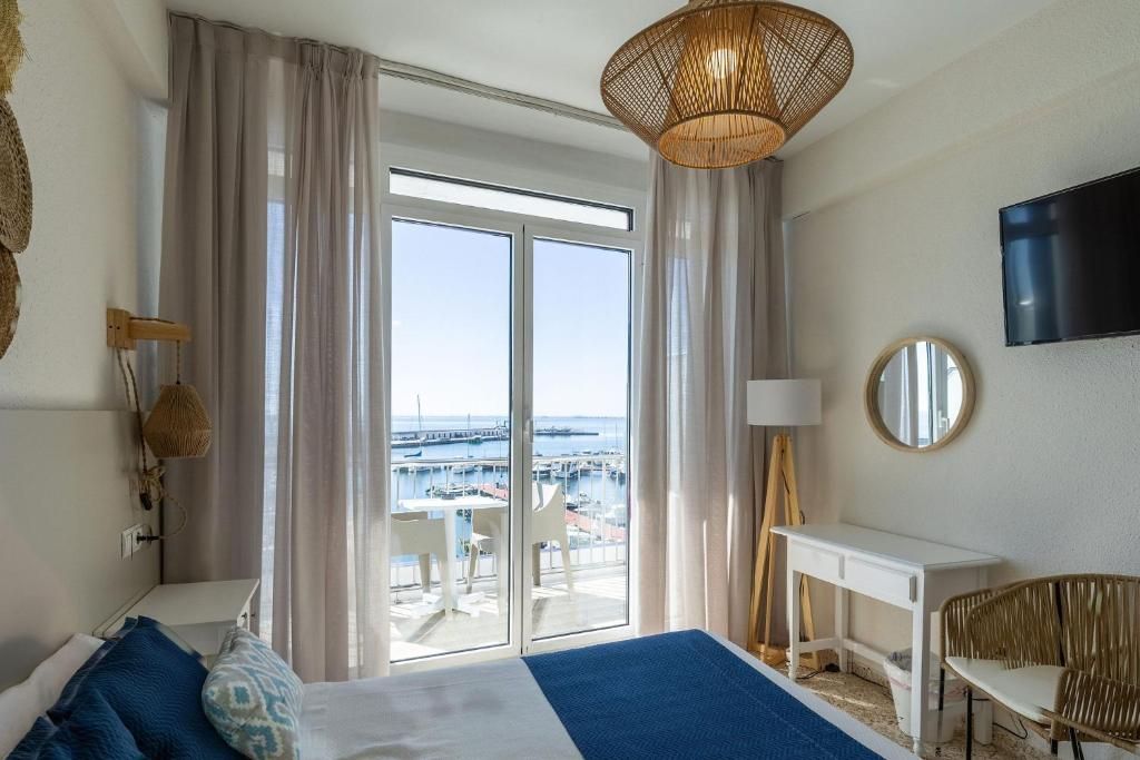 A hotel room with a bed, a desk, a chair, a TV, and a view of the marina.