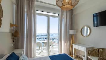 A hotel room with a bed, a desk, a chair, a TV, and a view of the marina.