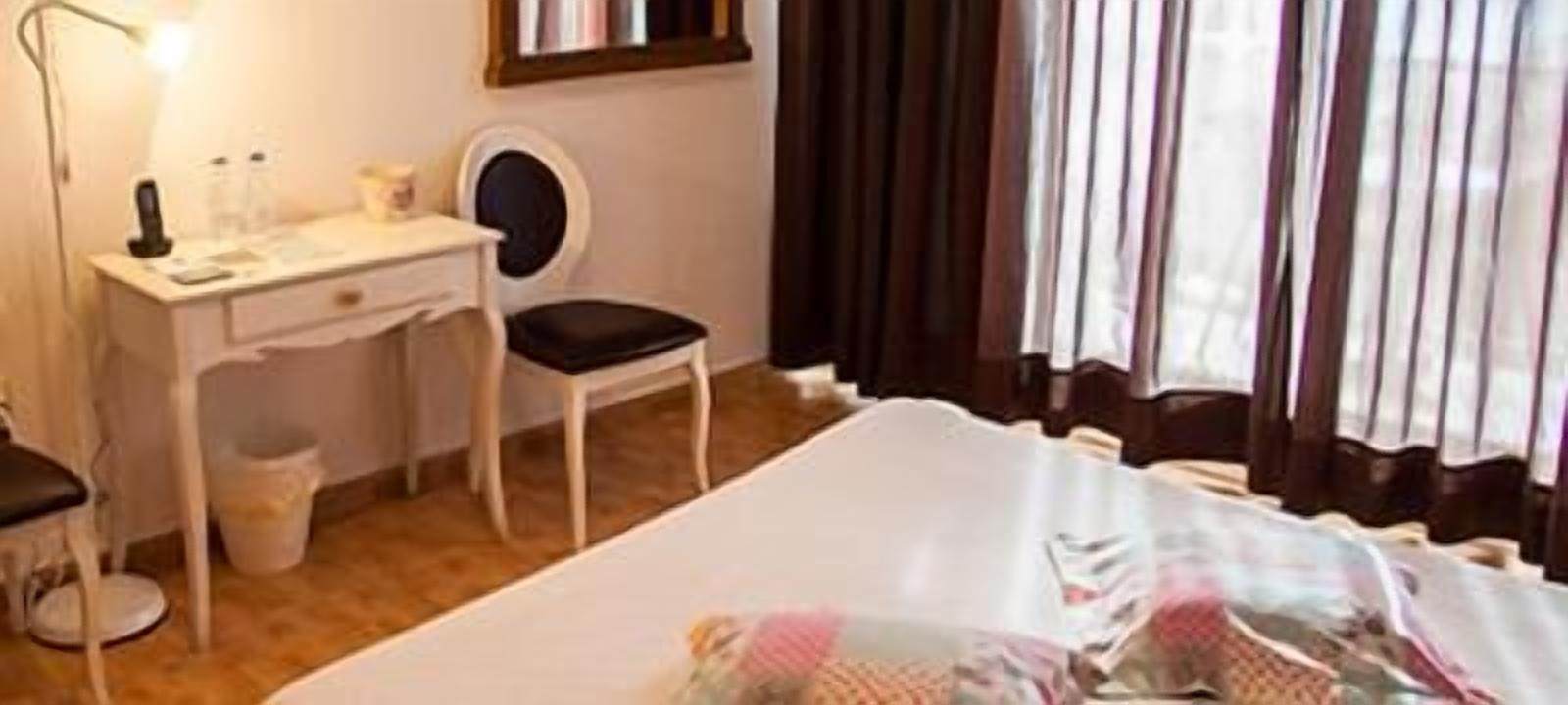 A hotel room with a bed, a desk, a chair, a lamp, and a window with curtains.