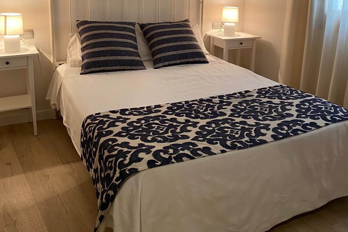 A neatly made bed with a patterned bedspread, two pillows, and a painting of sailboats above it.