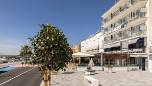 A hotel with a prominent 'H' sign, outdoor seating, and a clear view of the marina in the background. - Hotel Ampolla Sol (L'Ampolla)