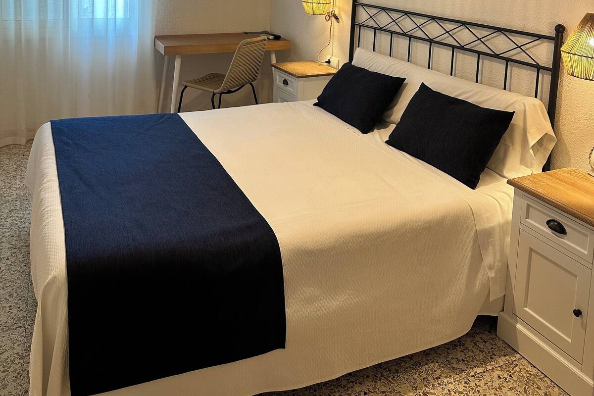 A neatly arranged hotel room with a bed, bedside table, lamp, and a desk with a chair.
