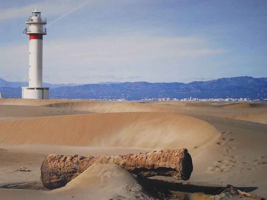 A lighthouse on a sandy beach with a clear sky and mountains in the background.