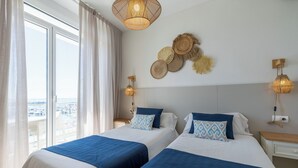 A hotel room with two beds, a large window with curtains, a view of the city, and decorative wall hangings. - Hotel Ampolla Sol (L'Ampolla)