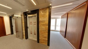 Un couloir d’hôtel au design moderne, avec un mur lambrissé en bois, un mur recouvert de carreaux de marbre et une porte d’ascenseur en verre.