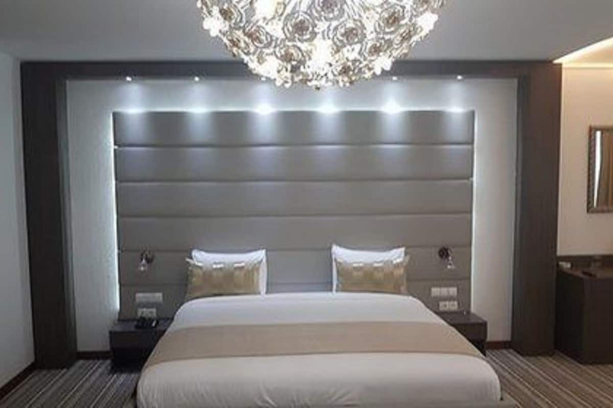 A modern hotel room with a large bed, a decorative chandelier, and a built-in headboard.