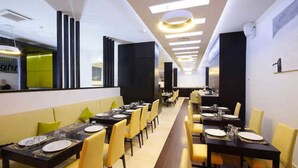 Un restaurant moderne avec de longues tables communes et des chaises jaunes, et un intérieur lumineux et épuré.