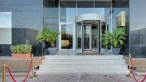 Une entrée moderne avec une porte tournante, des plantes en pot et un tapis rouge menant à l’entrée.