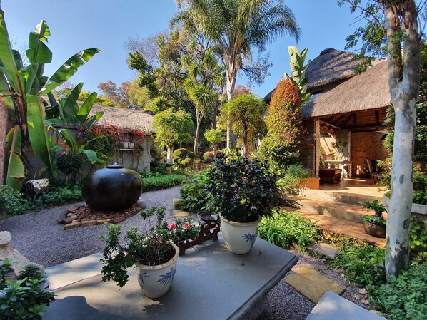 A garden with potted plants, a large decorative bowl, and a rustic building with a thatched roof.