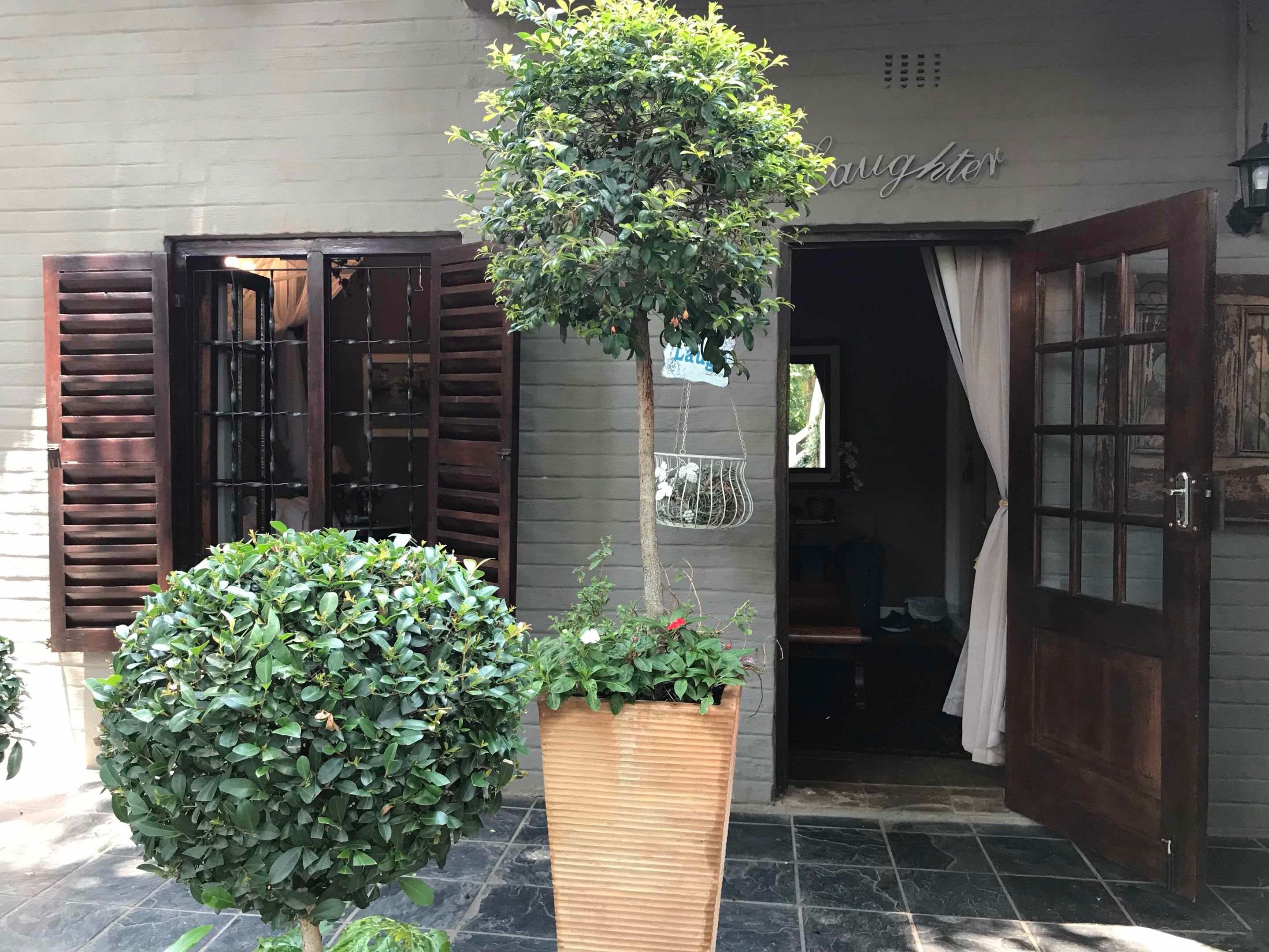 A hotel entrance with a wooden door, a large potted plant, and a hanging sign above the door.