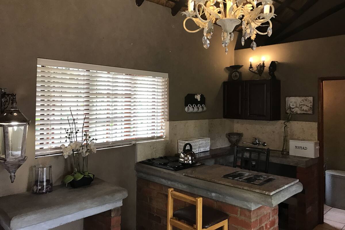A kitchen with a brick island, a chandelier, a window with blinds, and a clock on the wall.