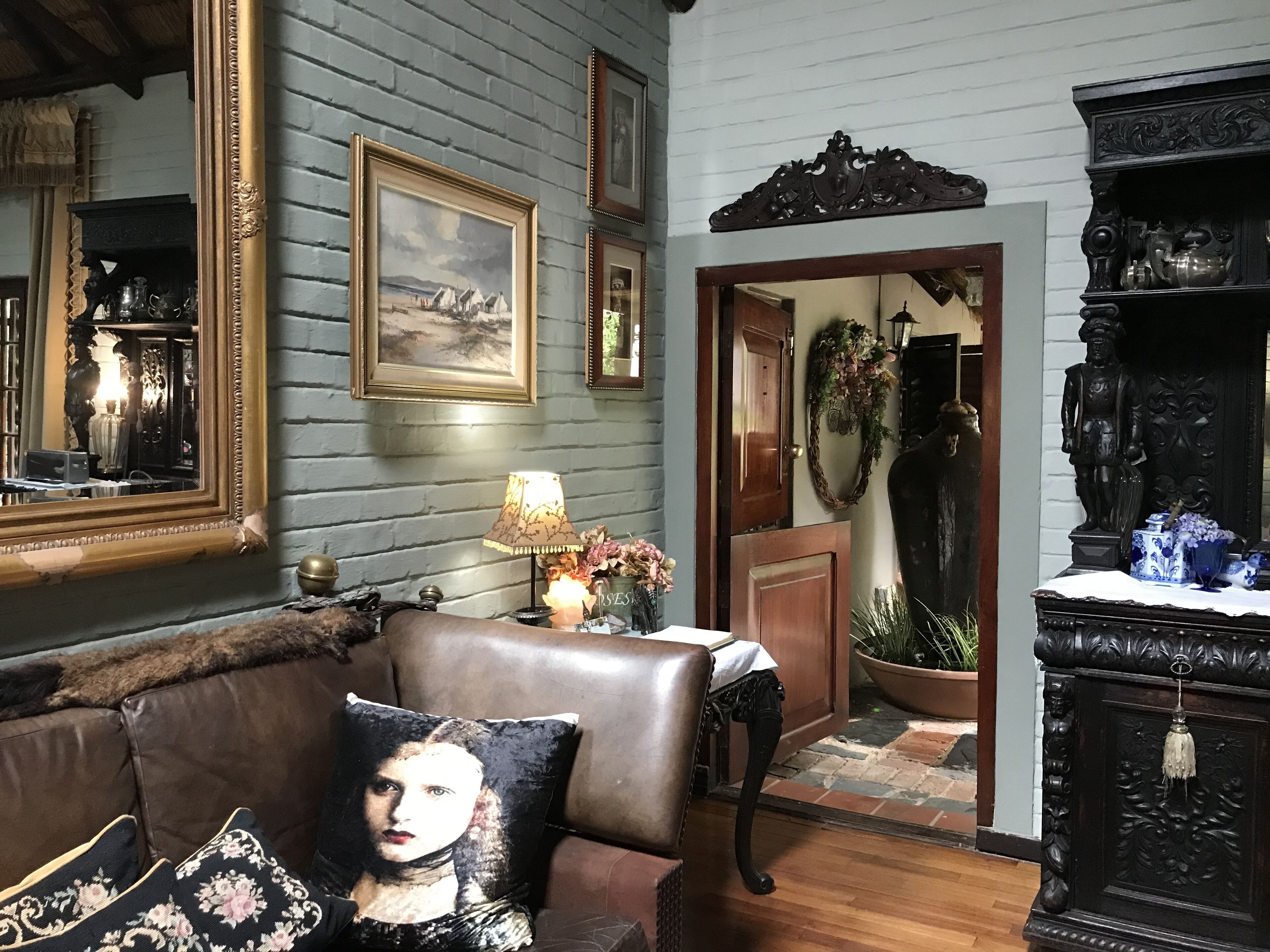 A room with a brown leather sofa, a wooden side table with a lamp, a framed painting, and a statue.