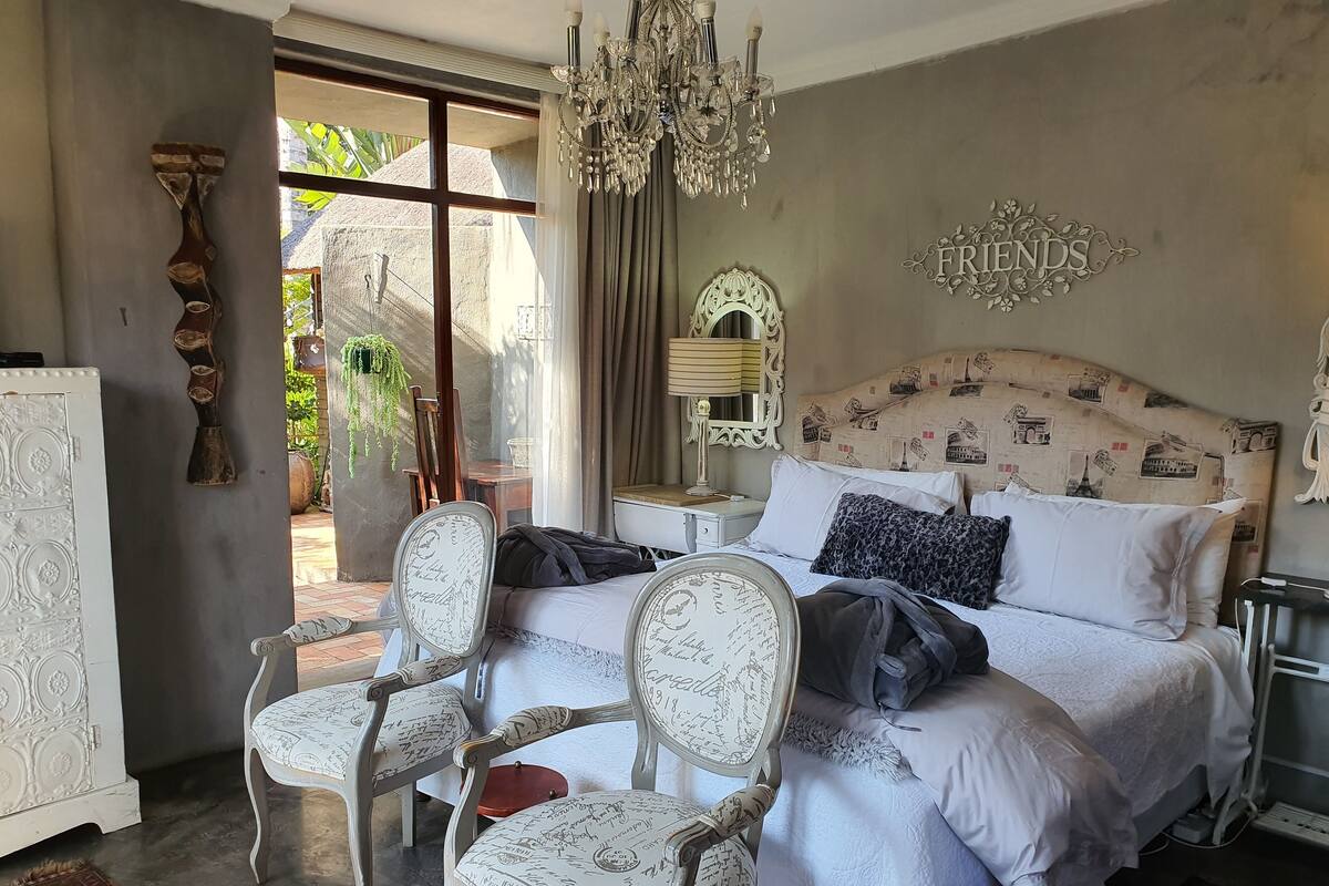 A bedroom with a bed, two chairs, a chandelier, and a 'FRIENDS' sign.