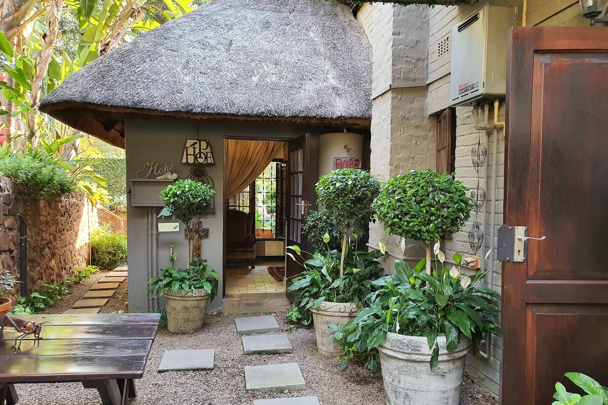 A cozy courtyard with a thatched-roof structure, potted plants, and a wooden bench.
