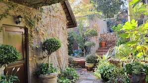 A rustic garden with a stone wall, potted plants, and a wooden door. - Waterhouse Guest Lodges 202 Lawley Street (Pretoria)
