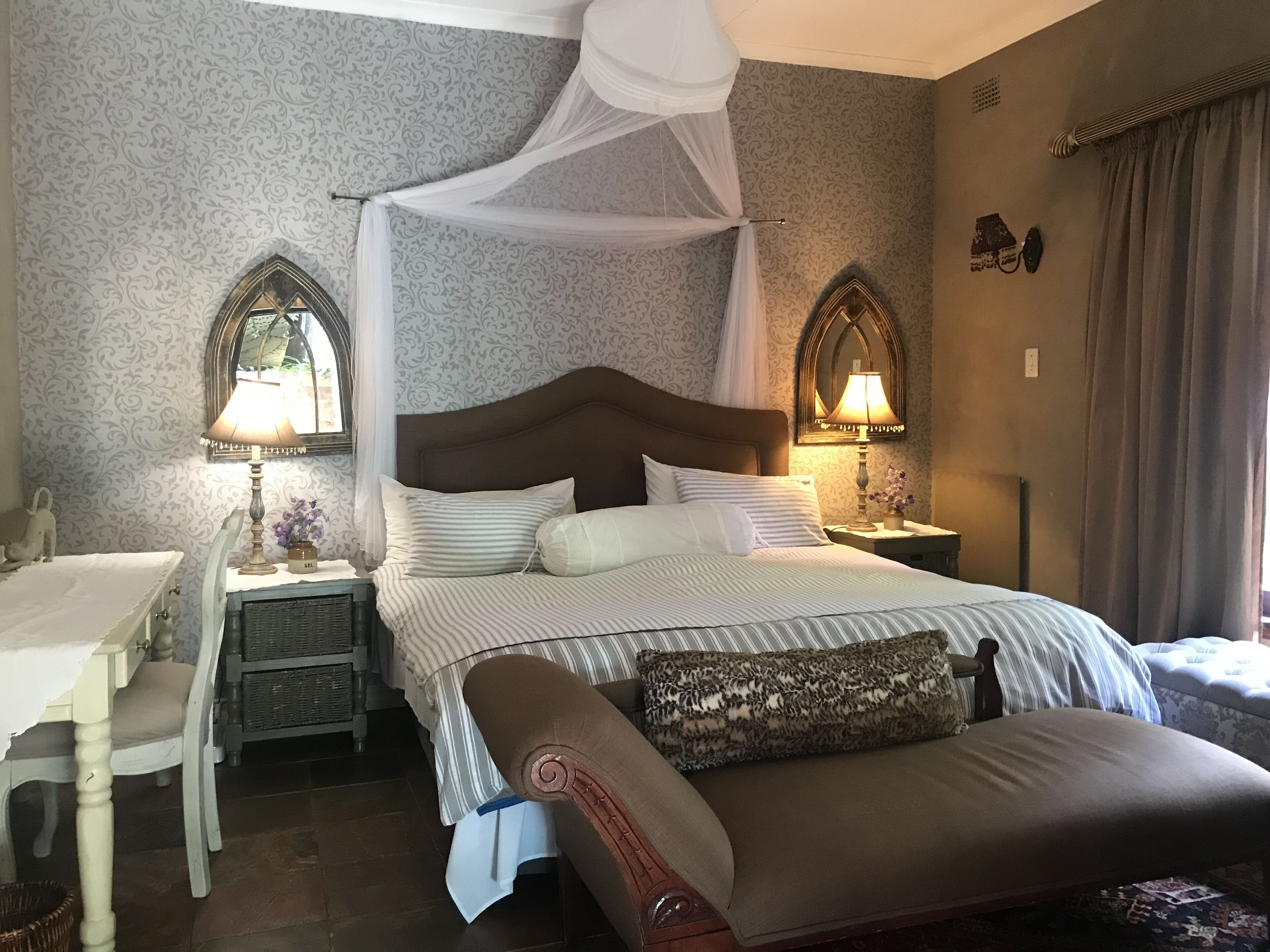 A bedroom with a four-poster bed, two bedside tables with lamps, a chair, and a small table with a lamp.
