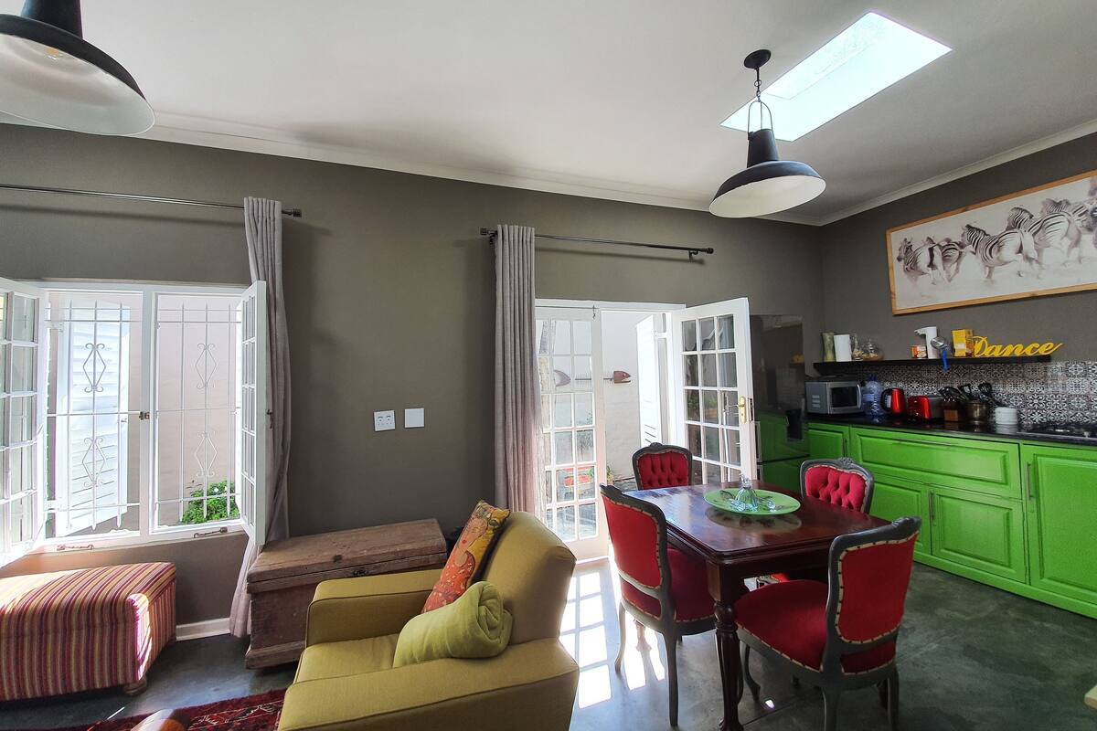 A dining area with a wooden table and red chairs, a sofa with a green cushion, and a kitchen area with green cabinets and a microwave.