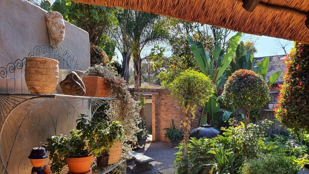 A garden with potted plants, a stone head sculpture, and a brick wall. - Waterhouse Guest Lodges 202 Lawley Street (Pretoria)