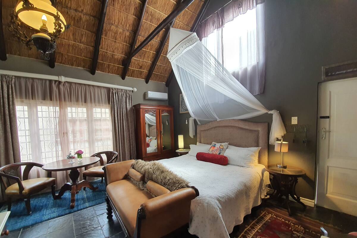 A room with a bed, a wooden cabinet, a table with chairs, and a ceiling fan.