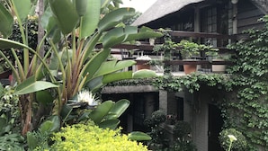 A traditional thatched-roof building with multiple balconies, surrounded by lush greenery and potted plants. - Waterhouse Guest Lodges 202 Lawley Street (Pretoria)