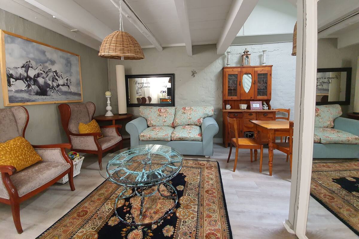 Ein Wohnzimmer mit einer Couch, Sesseln, einem Glastisch, einem Holzschrank und einem Bild an der Wand.