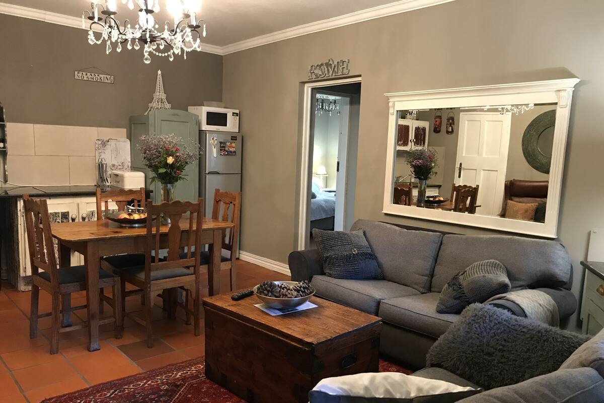 Ein Wohnzimmer mit einer Couch, einem Couchtisch und einem Essbereich mit Stühlen und einem Tisch. Es gibt eine Küchenzeile mit Kühlschrank und Mikrowelle.