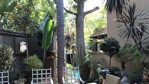 A patio with a wooden table, wicker chairs, potted plants, and a white fence. - Waterhouse Guest Lodges 295 Indus Street (Pretoria)