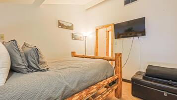 Une chambre à coucher avec un lit, une tête de lit en bois, un téléviseur fixé au mur et une valise posée sur le sol.