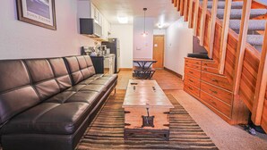 Una sala de estar con un sofá de cuero, una mesa de centro, un aparador de madera y una escalera.