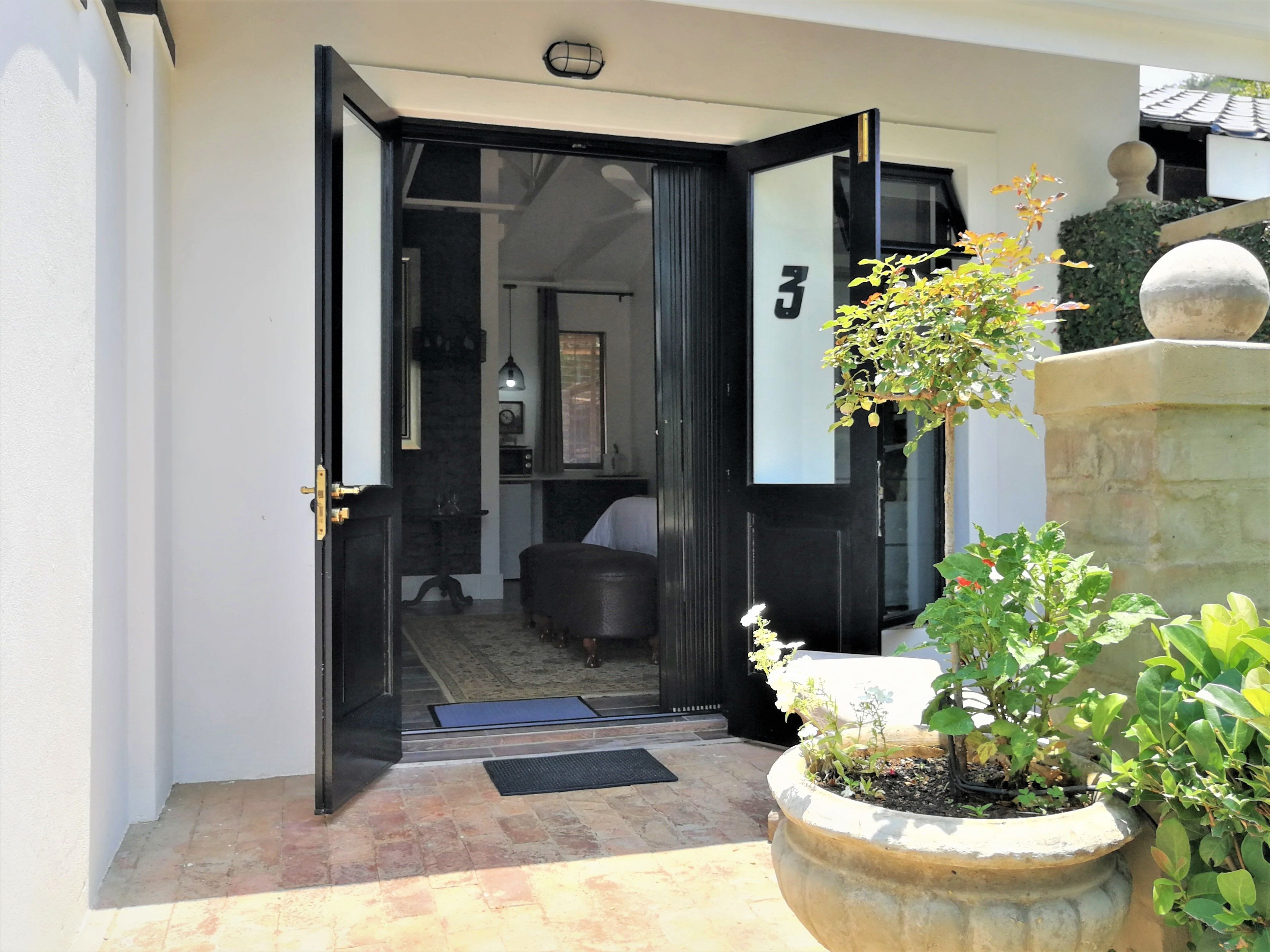 Uma entrada moderna com porta de vidro, placa com o número 3, um pequeno espaço de estar interno e uma planta em vaso.