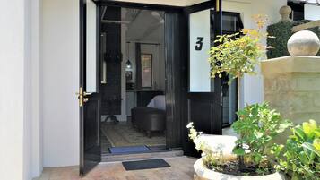 Uma entrada moderna com porta de vidro, placa com o número 3, um pequeno espaço de estar interno e uma planta em vaso.