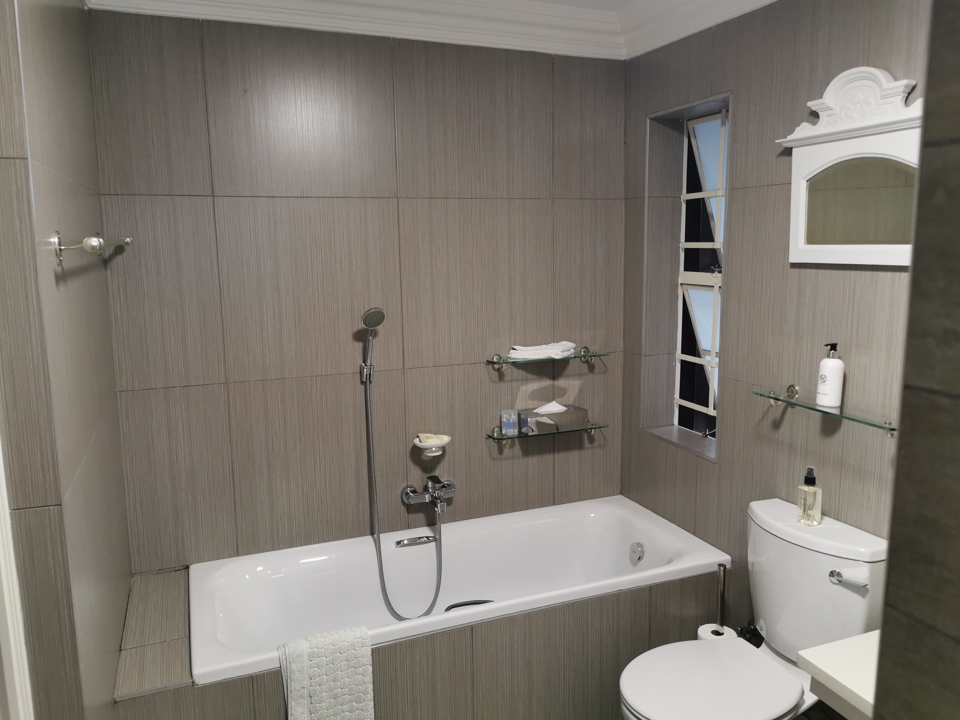 Un baño moderno con bañera, inodoro y estantes de vidrio con artículos de aseo.