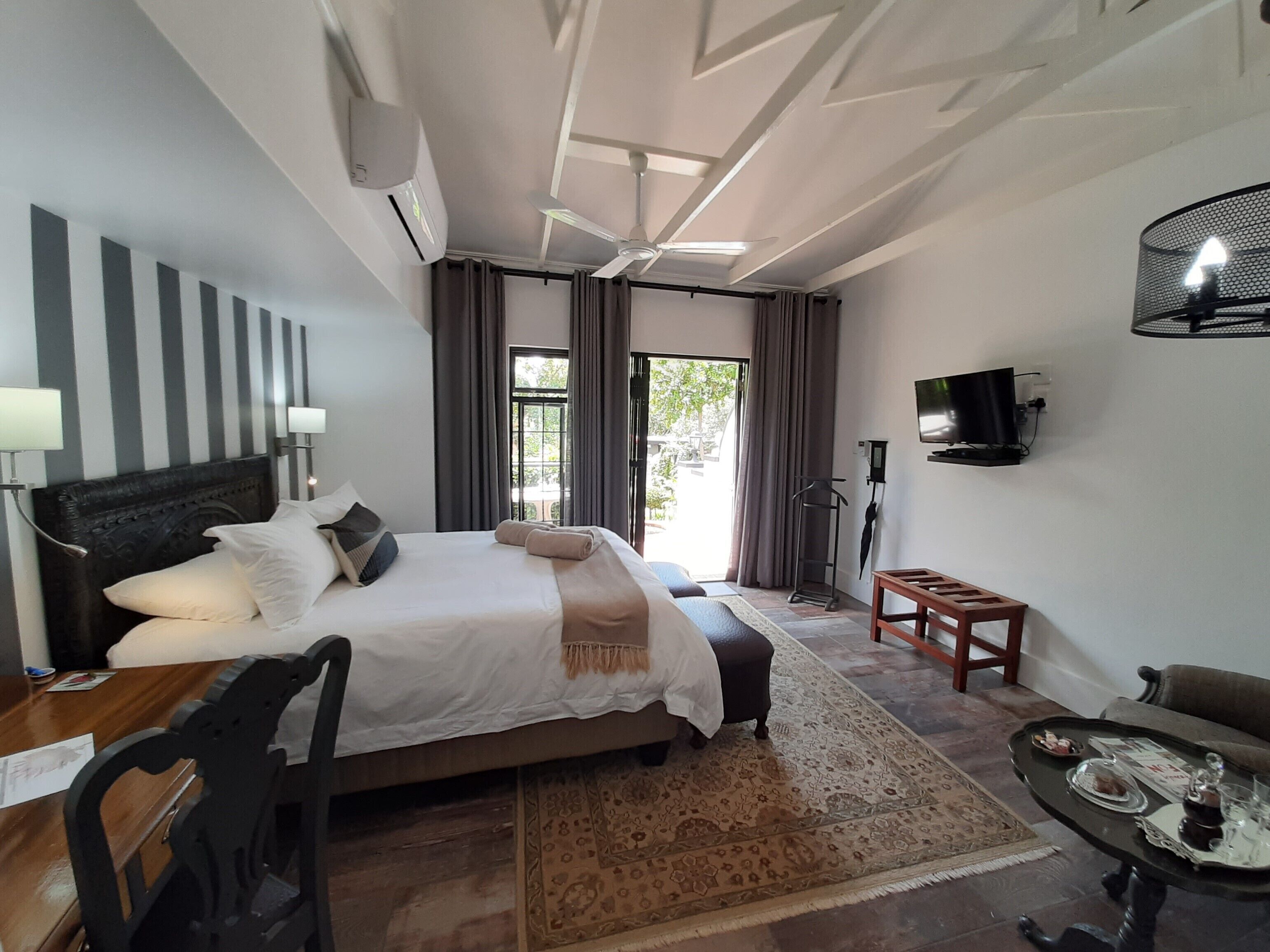 Quarto de hotel com uma cama grande, uma escrivaninha, uma cadeira, uma televisão e vista para o exterior.