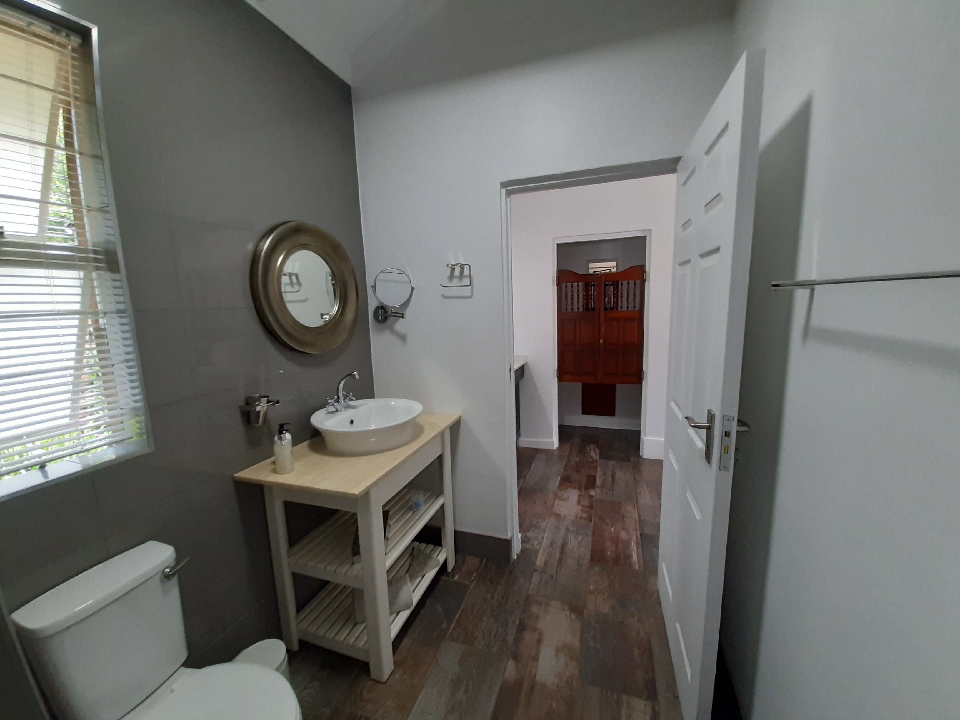 A bathroom with a toilet, sink, mirror, and wooden vanity.
