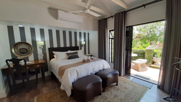 Habitación de hotel con cama, escritorio, silla, ventilador de techo y vistas al exterior.
